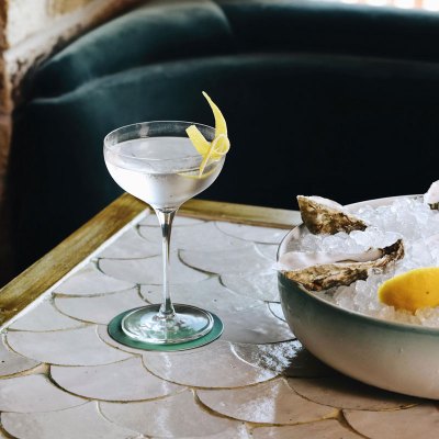 Vodka martini with a thin slice of lemon sits beside plate of oysters sat on ice