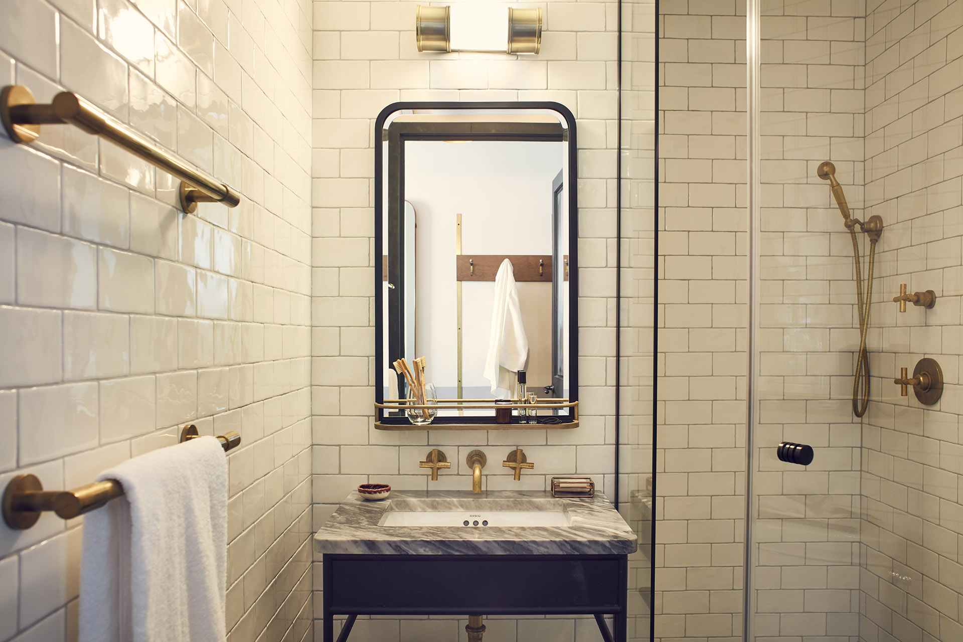 The ensuite bathroom has white tiling and gold fittings, with a large mirror above the sink