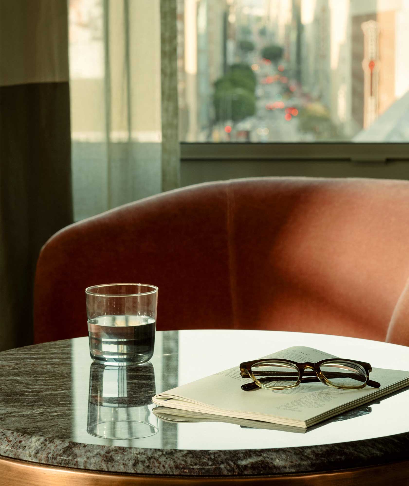 A glass of water, pair of reading glasses and a book sit on the table in the guest room