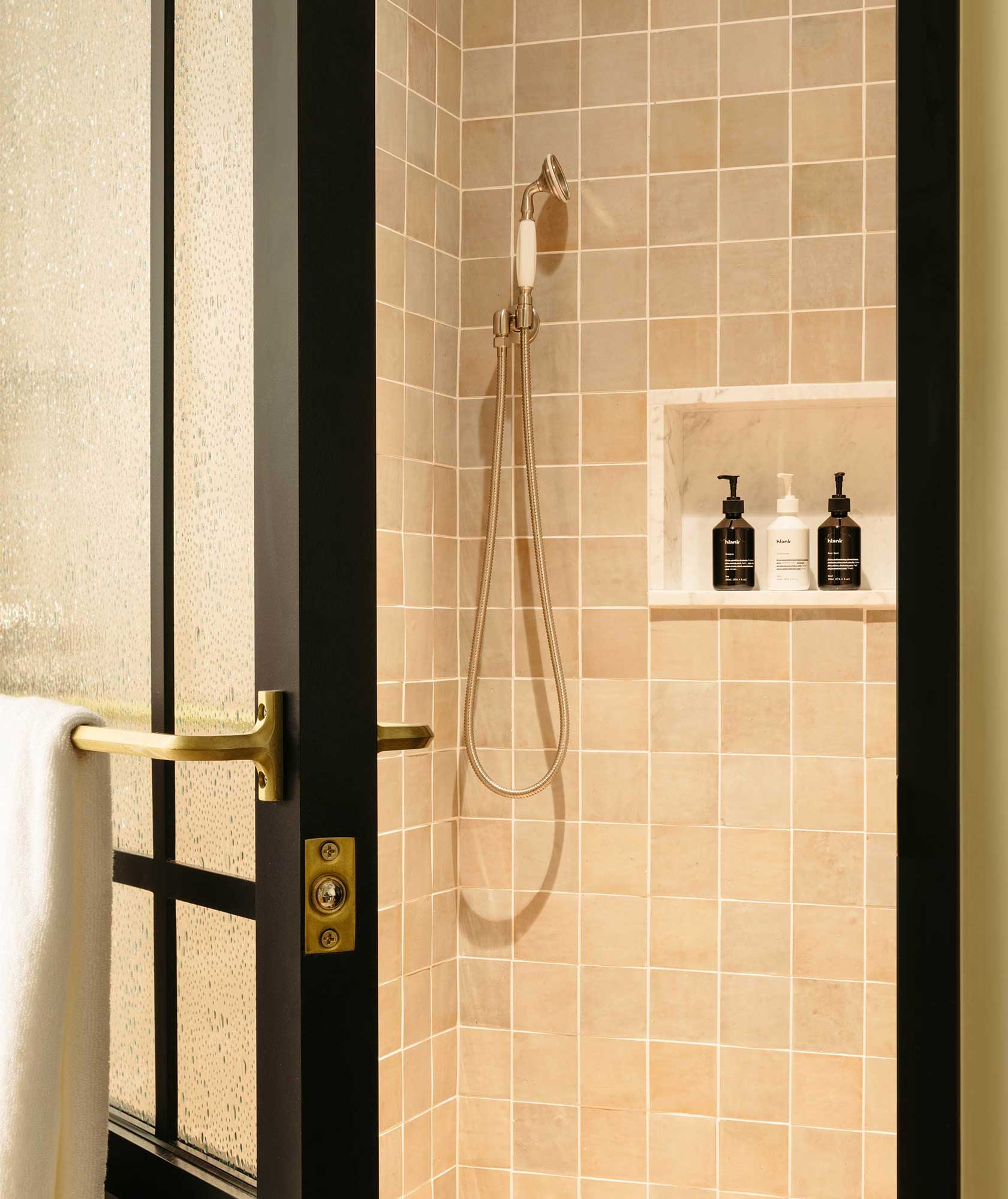 The shower door has a white towel hanging on it, with shower gel, shampoo and conditioner in the shower itself.
