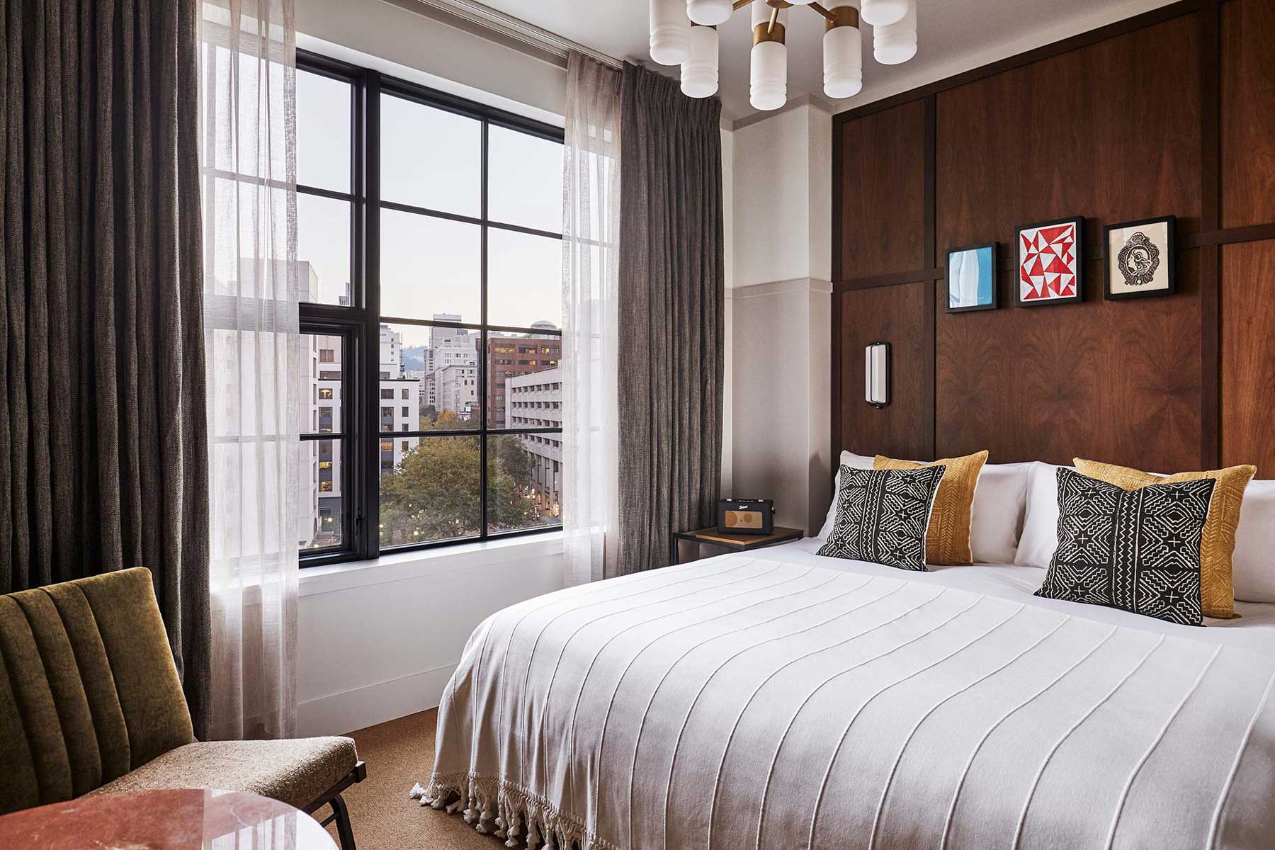 Queen sized bed beside a large window that shows a stunning view of the city