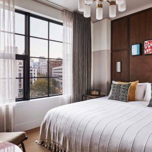 Queen sized bed beside a large window that shows a stunning view of the city