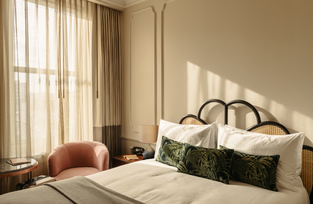 Cozy Queen room with a queen-size bed, large windows letting in abundant natural light, and a pink armchair with a side table.