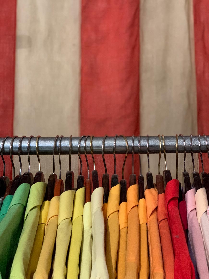 A rack of very brightly coloured shirts, from green through yellow, orange, red and pink