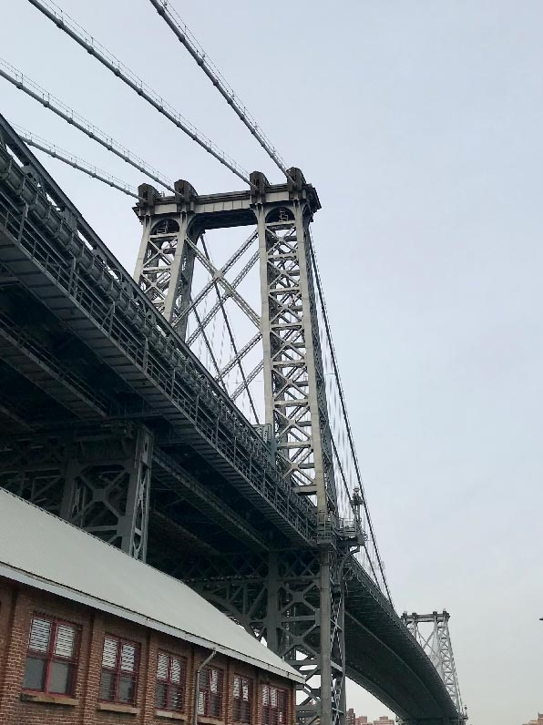 Looking up at the Williamsburg Bridge from the ground, on a grey-blue sky day