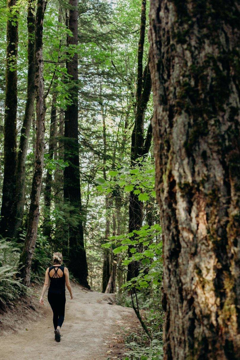 A girl walks on a path among tall leafy trees in Forest Park, Portland