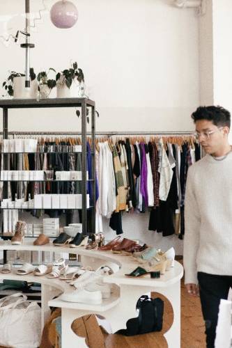 Un homme regarde des chaussures exposées devant des étagères et un long rail de vêtements.