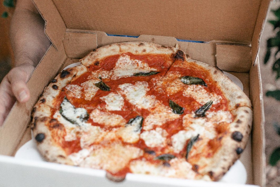 An open takeout box with pizza inside of it, with mozzarella and basil toppings