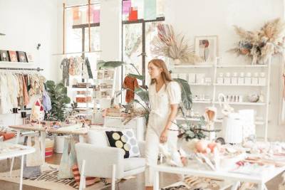 A person walks through a retail space with white walls selling various products such as clothing, candles and home furnishings