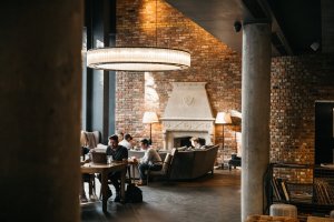 Large hanging circular light over people sitting in the hotel lobby, with an exposed brick wall and fireplace