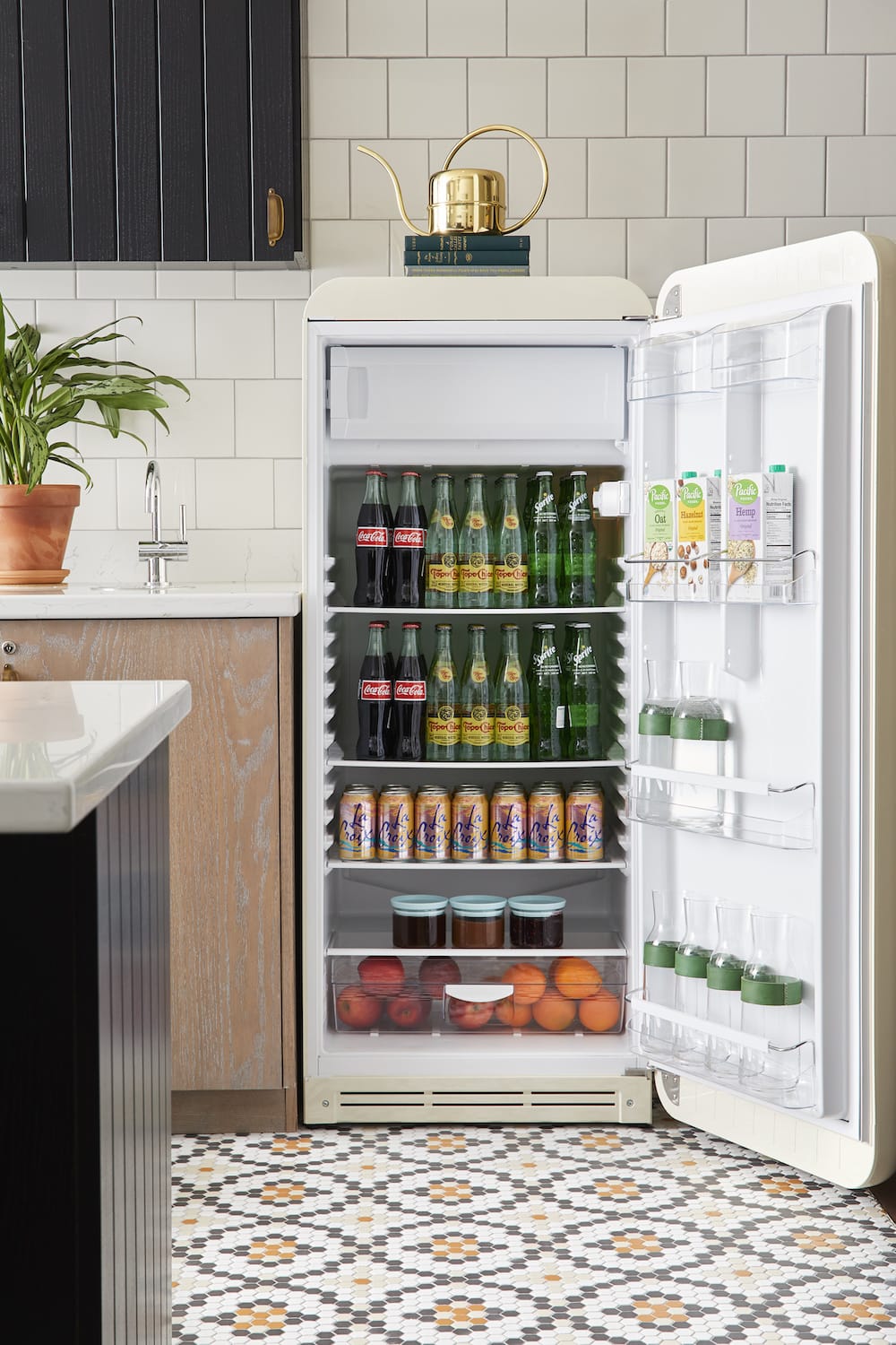 A large fridge with its door open, showing it's full of soft drinks, milk, water and fruit