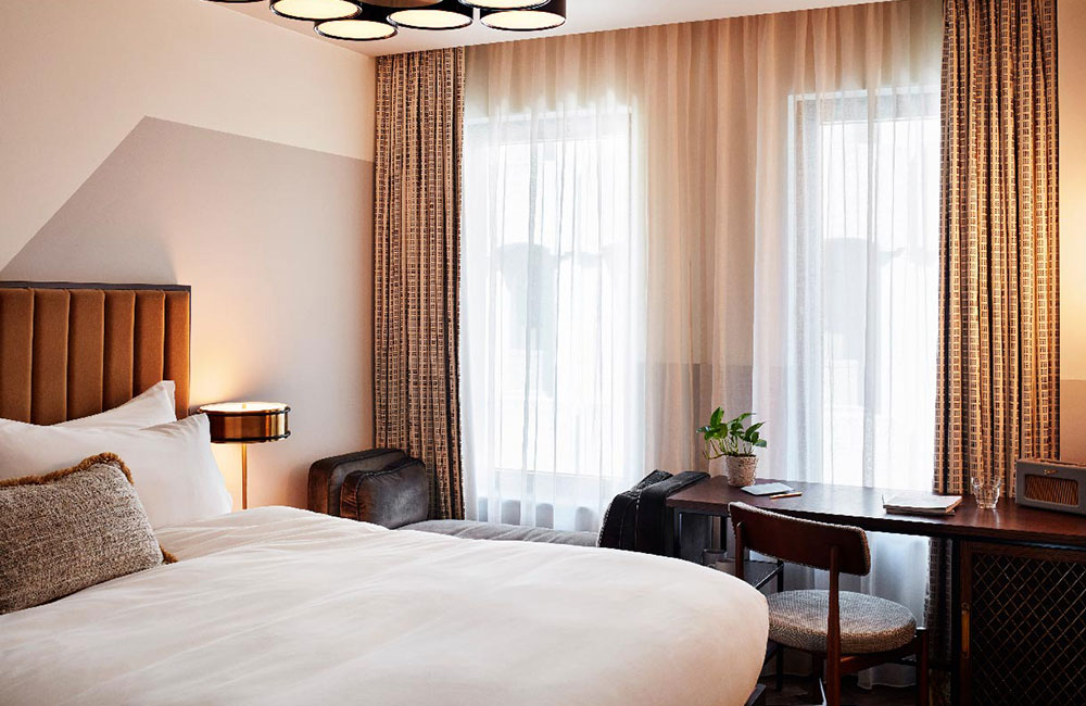 Large bright windows behind a two seater backless sofa and desk. Unlike the Cosy, the walls are plain colours.