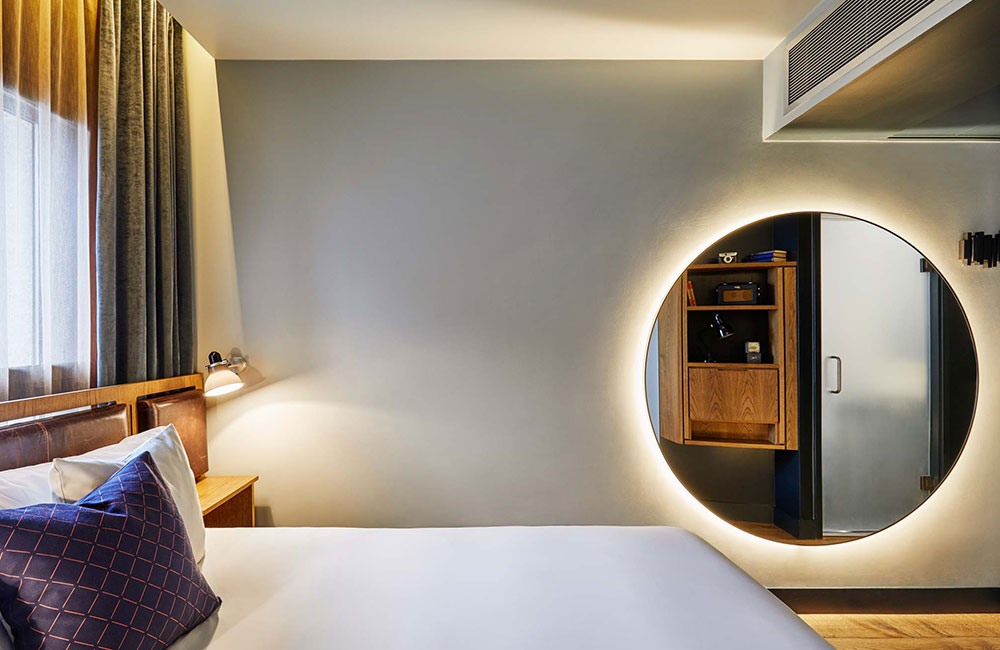 View from the side of the bed showing a large circular mirror on the wall
