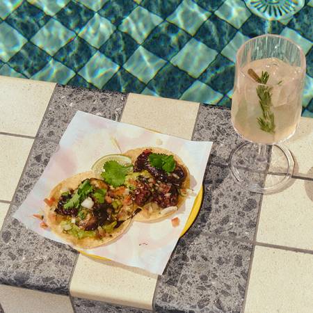 Pool edge with a tray of tacos and a refreshing beverage.