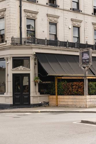 The Oak W12 exterior, a traditional London pub with dark awning and outdoor seating area.