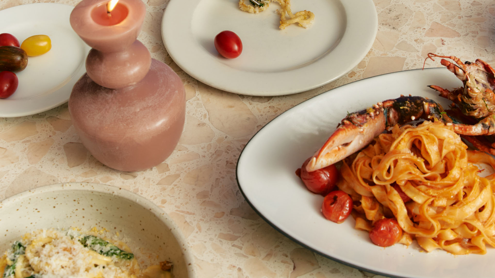 close-up of table with pasta dish and sides and decorative wax candle.