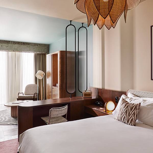 Sunlit interior of a bedroom containing comfy bed, wall art and open wardrobe.
