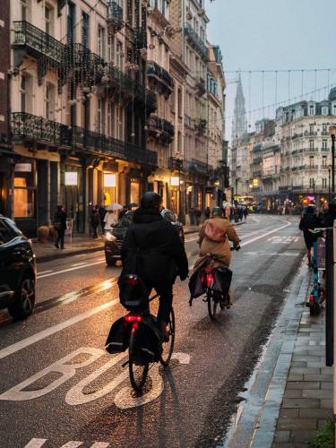 La lumière du crépuscule se reflète sur la chaussée humide de la rue Antoine Dansaert, avec trois cyclistes au premier plan.