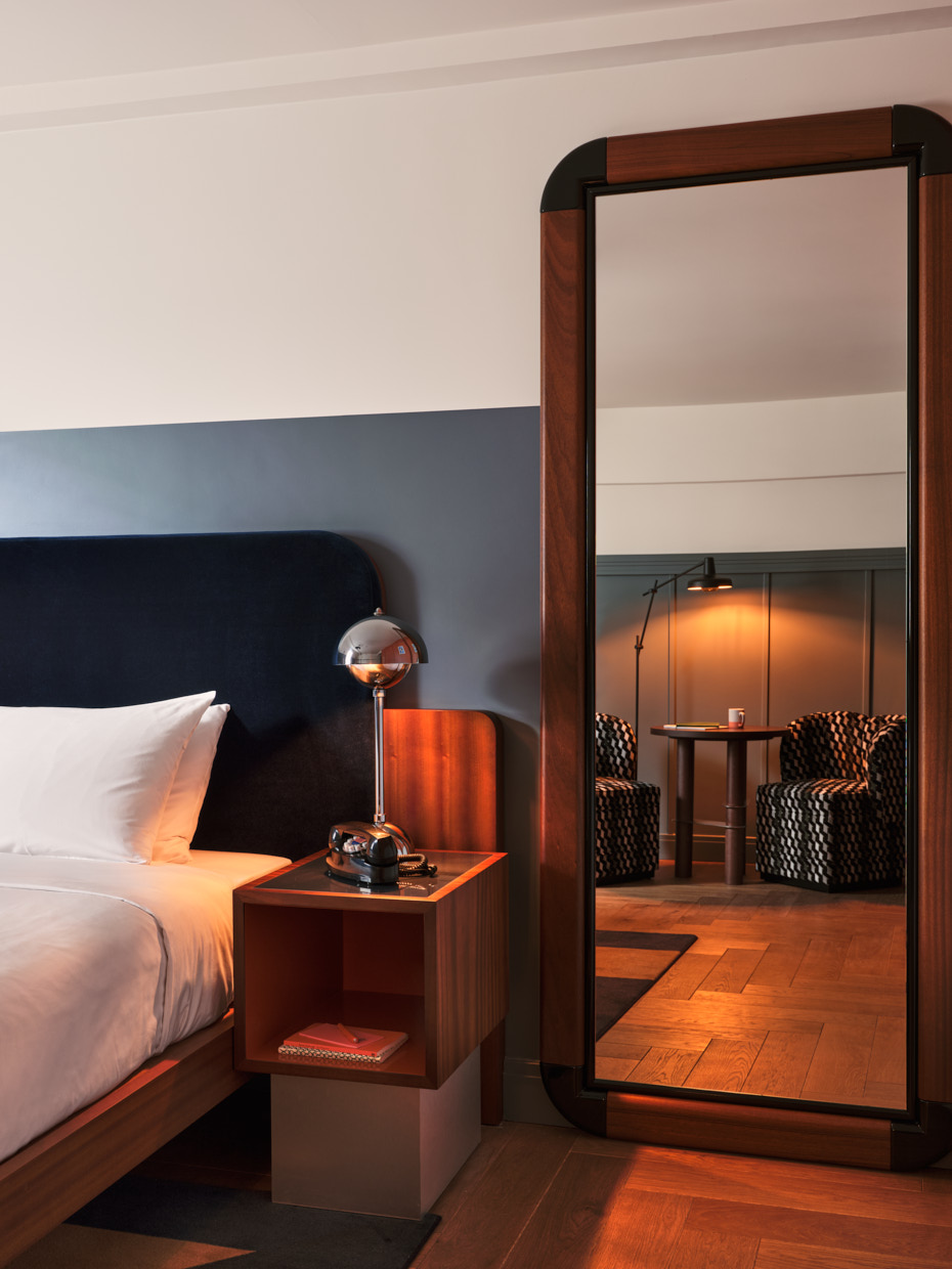 Tall mirror by bedside table reflects lamplight