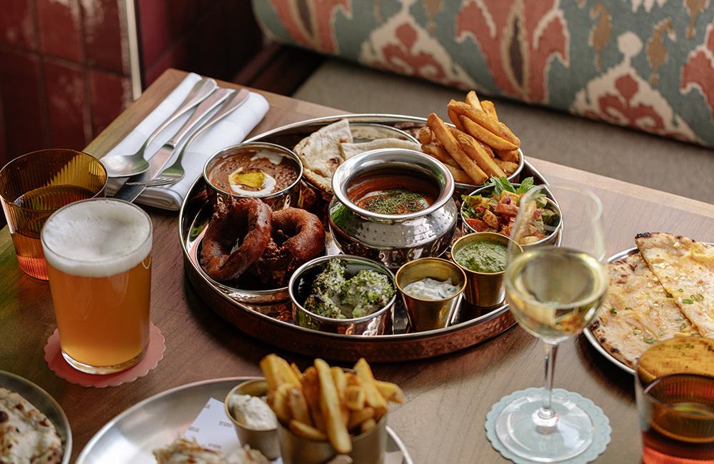 Beer and wine with a round tray of tasty Indian cuisine between them.