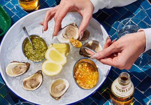 Tray of oysters on a bed of ice with lemon and a bottle of beer.