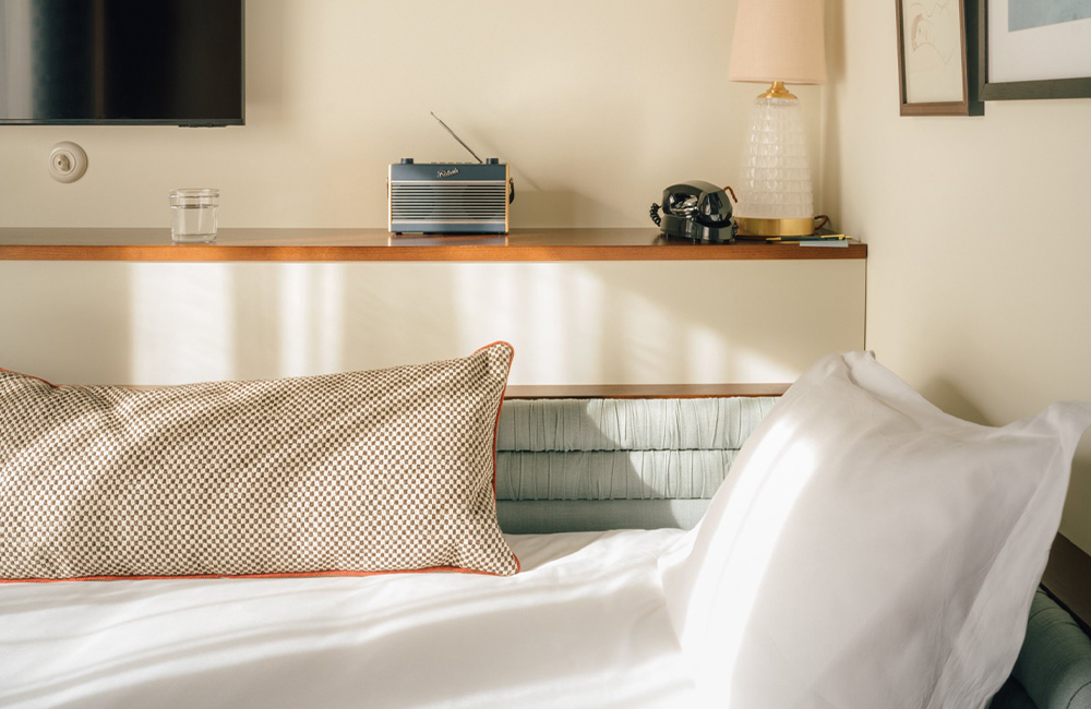 side view of single bed in corner, with a pillow and bolster cushion.