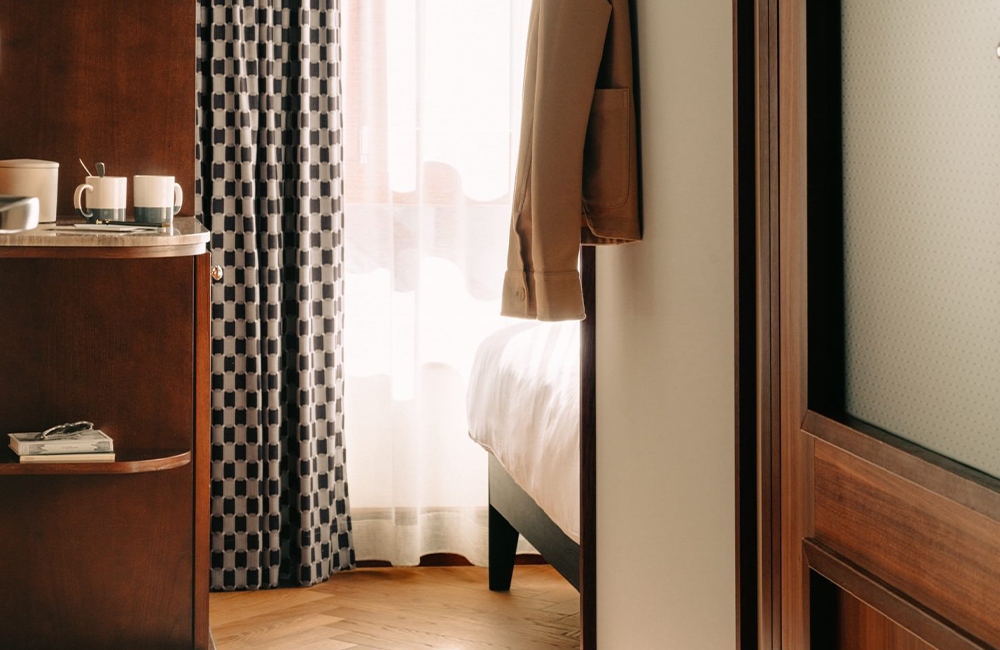 Low view of the entrance of the shoebox room, with a small corner shelf with mugs and a glint of the bed.