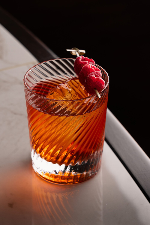 delicious deep orange iced cocktail in a low glass with raspberry garnish.