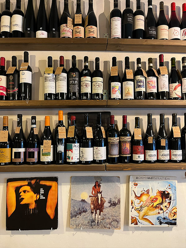 Shelves displaying a variety of bottles of wine and some art work hanging on the wall.