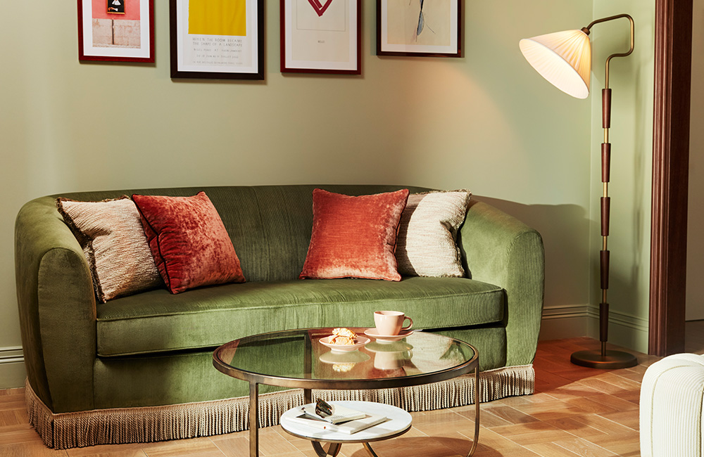 Large green soft velvet two-seater sofa against the wall, with a coffee table in front and a floor lamp nearby.