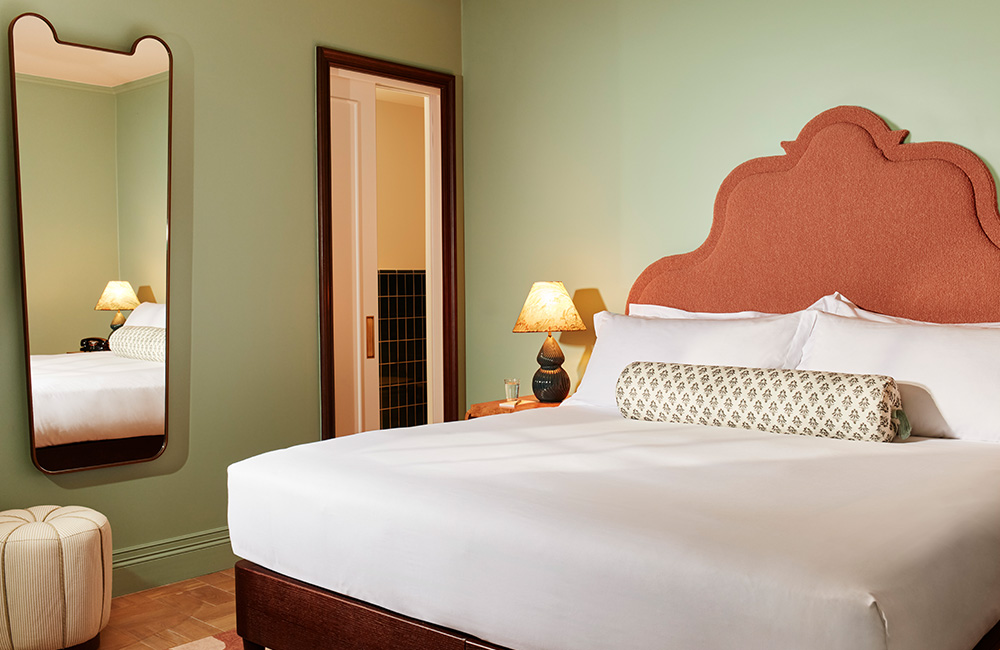 Large window, and natural sunlight illuminates a pink upholstered bed frame.