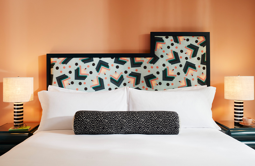 Large printed bolster on top of a bed, with black and white side lamps positioned on either side of the bed.