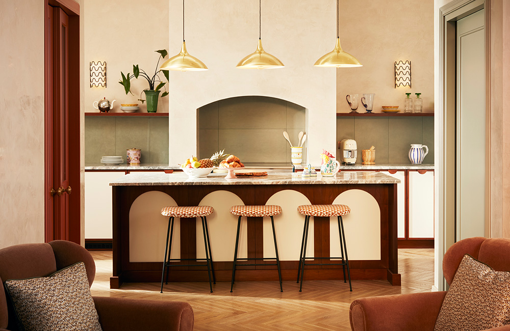 Large open-plan kitchen with natural light, featuring a marble-covered kitchen island with three patterned barstools, seamlessly connected to the living room.