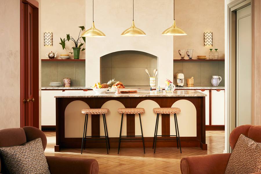 Large open-plan kitchen with natural light, featuring a marble-covered kitchen island with three patterned barstools, seamlessly connected to the living room.