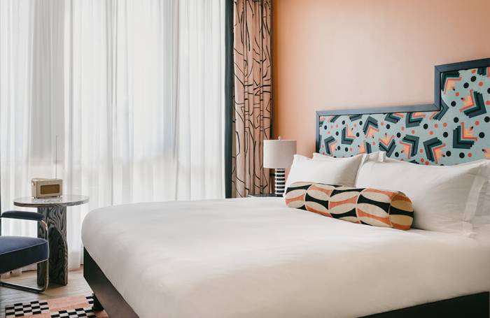 Side view of a coral-coloured cozy terrace with natural light illuminating a king-size bed, an armchair, and a side table in a corner.
