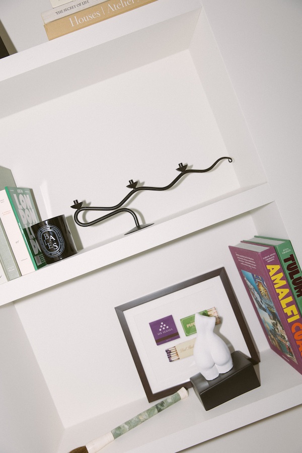 White bookcase showcasing several items, from books, candelabra, scented candle and so much more.- The Localist, Hoxton Hotels.